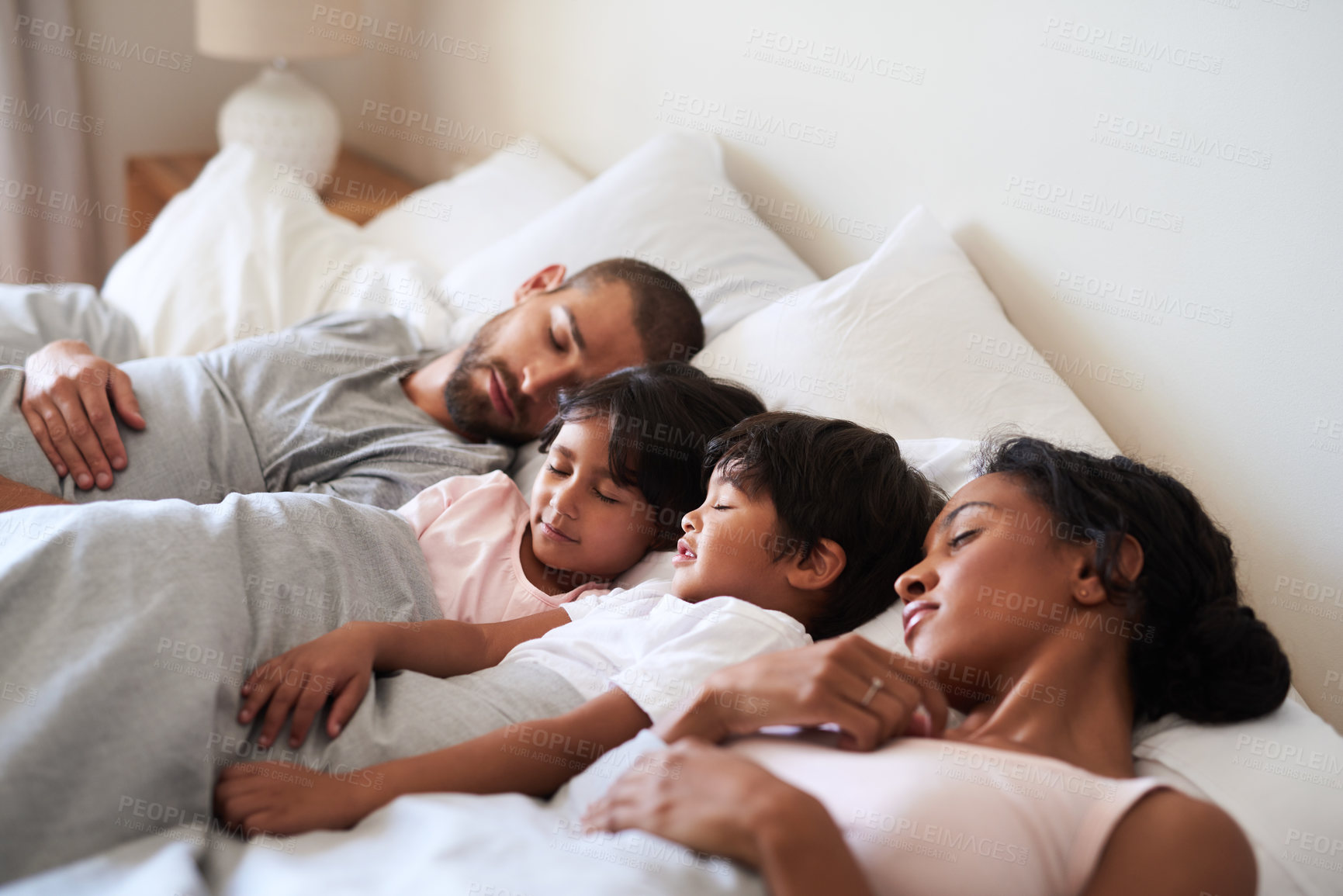 Buy stock photo Shot of a beautiful young family of four fast asleep in bed together in their bedroom at home