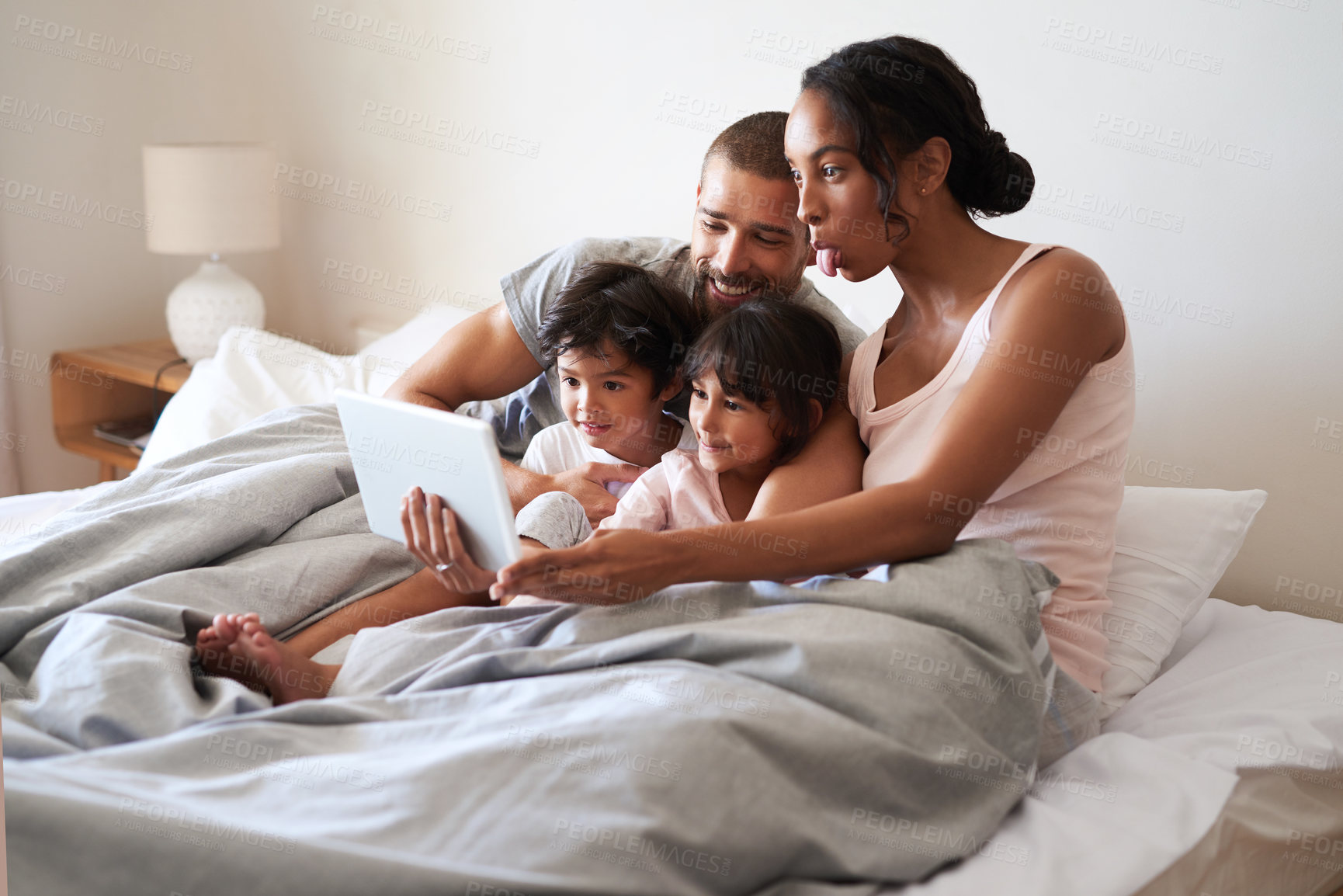 Buy stock photo Family, playful and tablet on bed for bonding, relax and streaming together with movie, video and app. Parents, smile and children as people in home bedroom for film, relationship or games on weekend