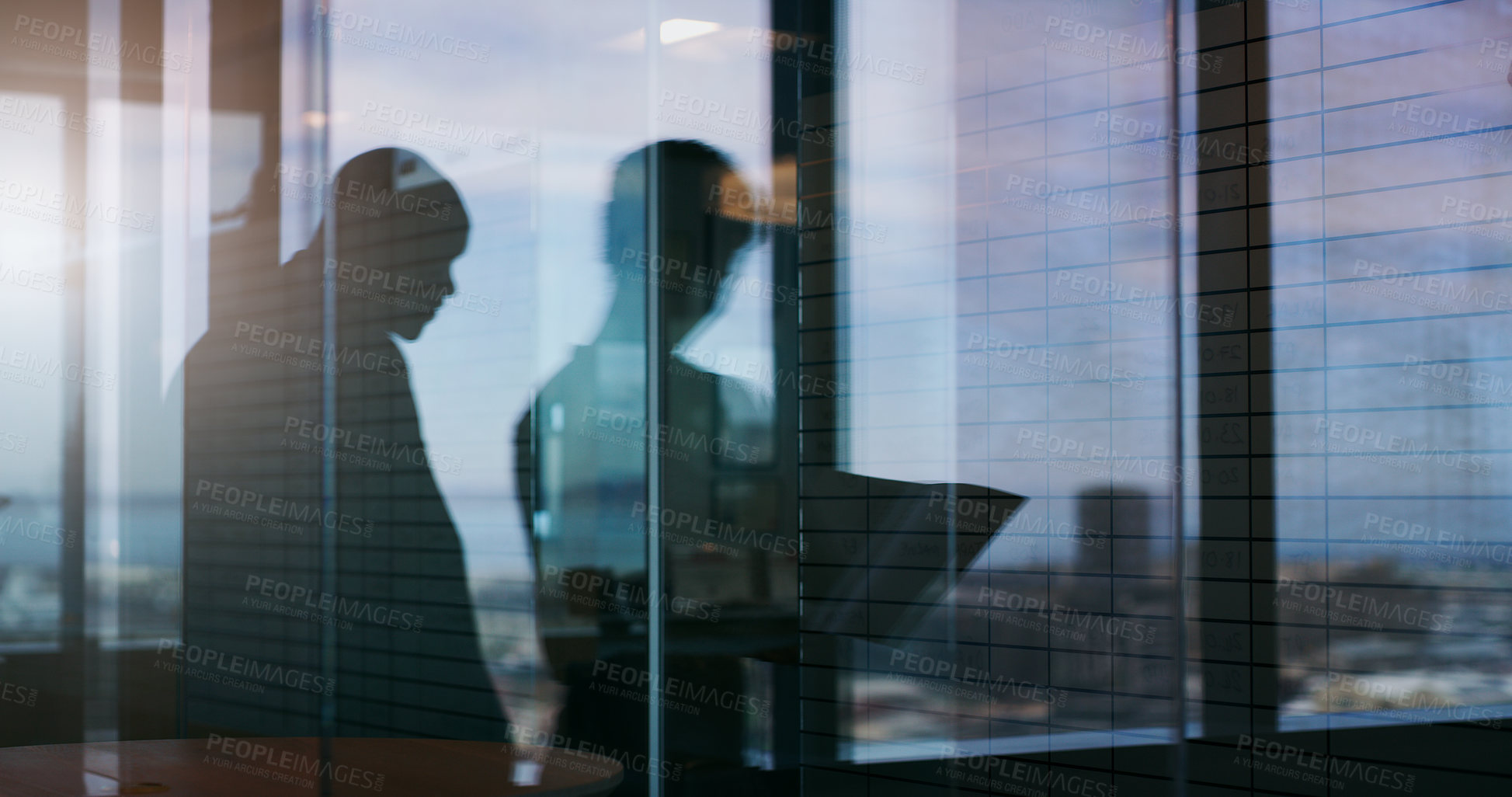 Buy stock photo Silhouette shot of two businesspeople having a discussion inside an office building