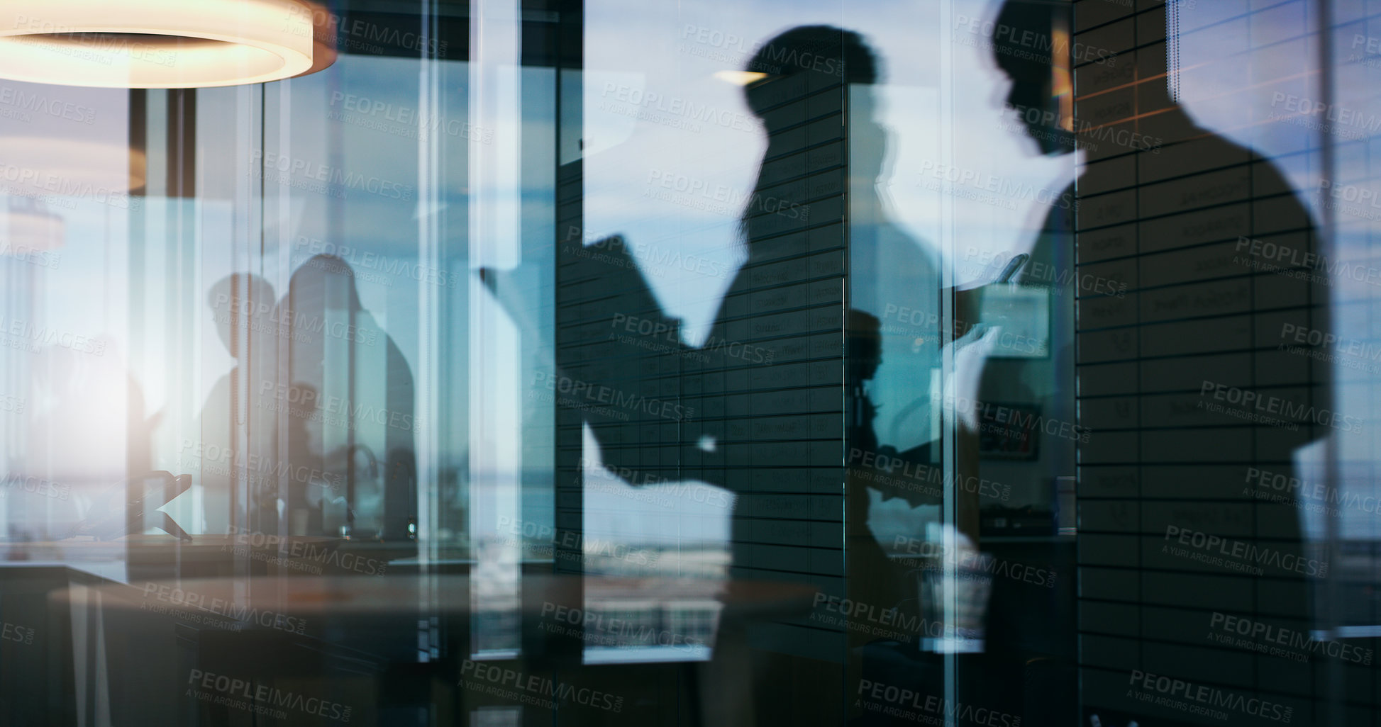 Buy stock photo Silhouette shot of two businesspeople having a discussion inside an office building