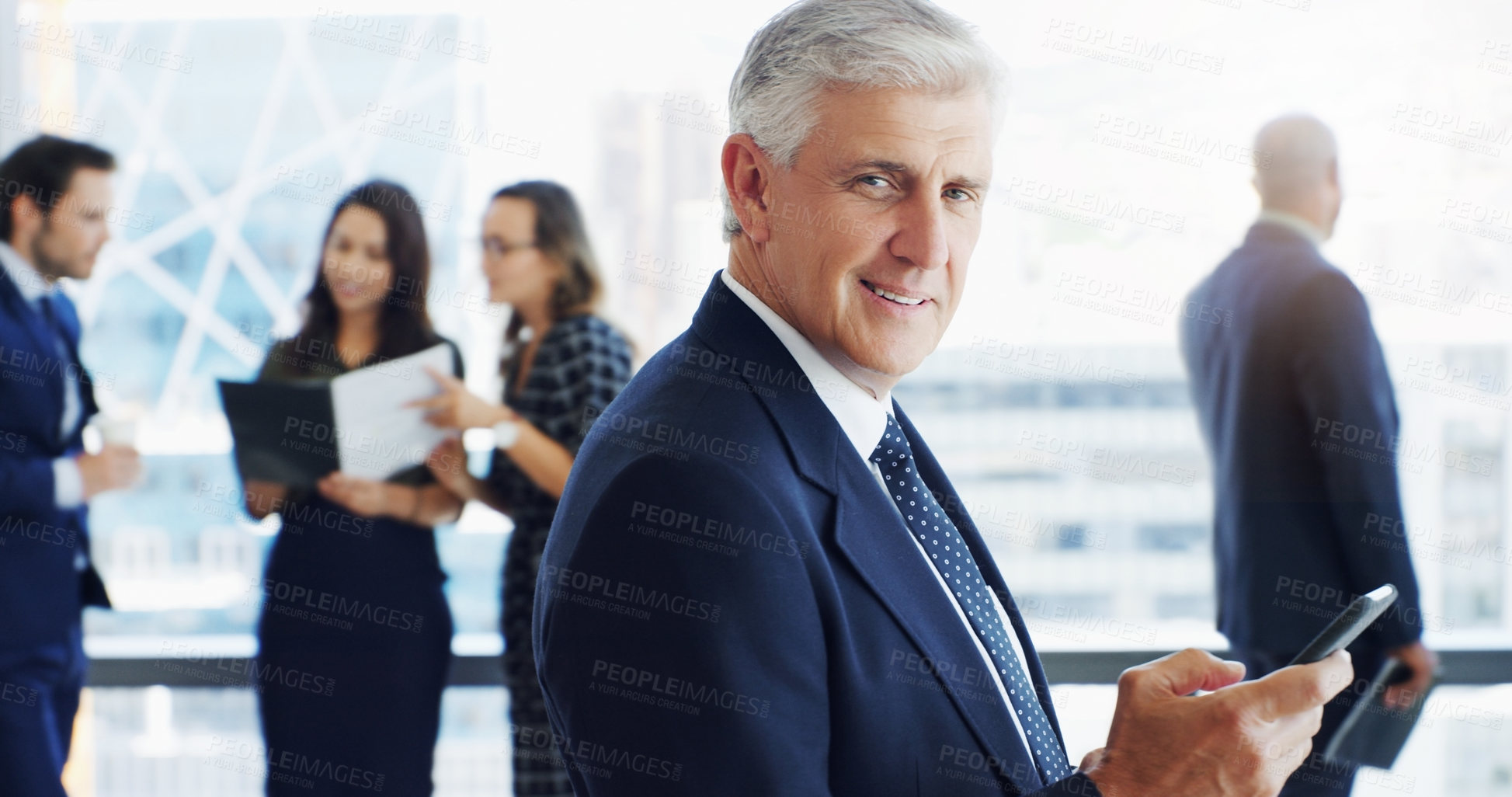 Buy stock photo Shot of a handsome businessman smiling at the camera while colleagues are blurred in the background