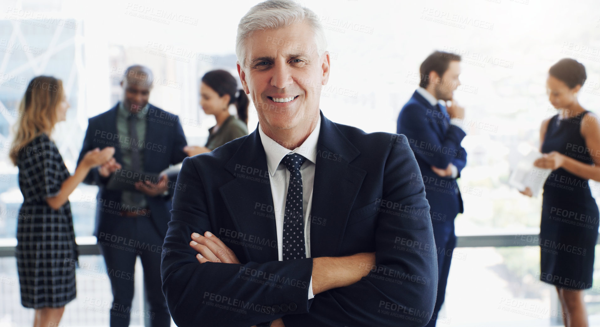 Buy stock photo Shot of a handsome businessman smiling at the camera while colleagues are blurred in the background