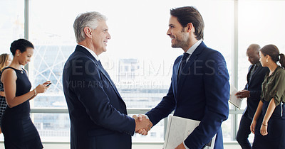 Buy stock photo Cropped shot of two businesspeople shaking hands while colleagues are blurred in the background
