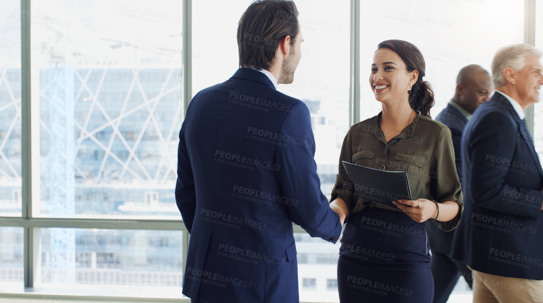 Buy stock photo Cropped shot of two businesspeople shaking hands while colleagues are blurred in the background