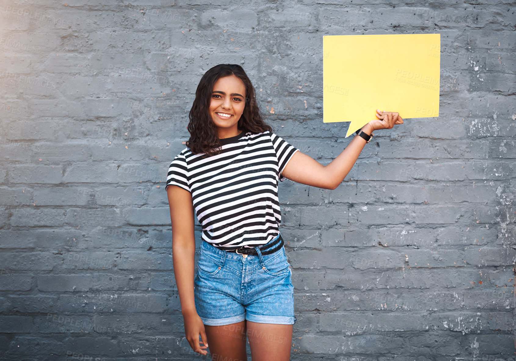 Buy stock photo Portrait of a young woman holding a speech bubble against a grey wall