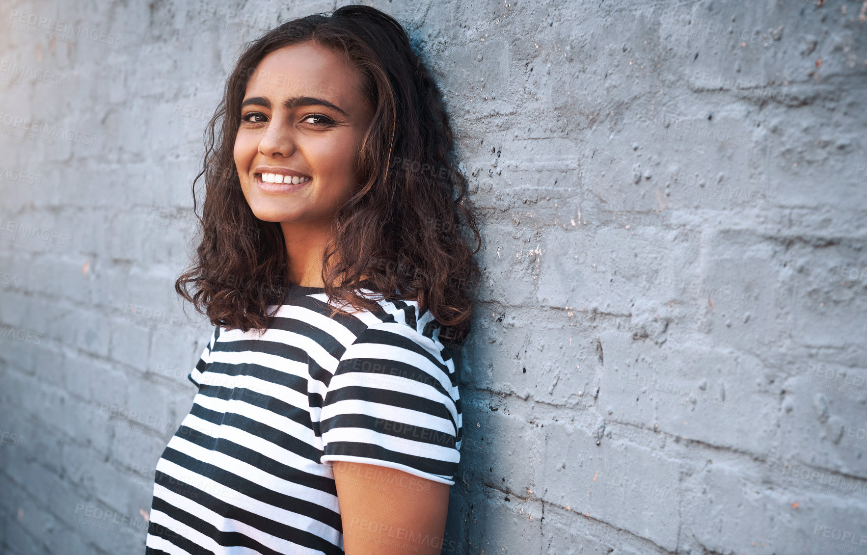 Buy stock photo Portrait, girl and smile on brick wall, outdoor and streetwear for happy, fashion and grey background. City, gen z and striped tshirt on hispanic model, casual and trendy clothes or confident, laugh