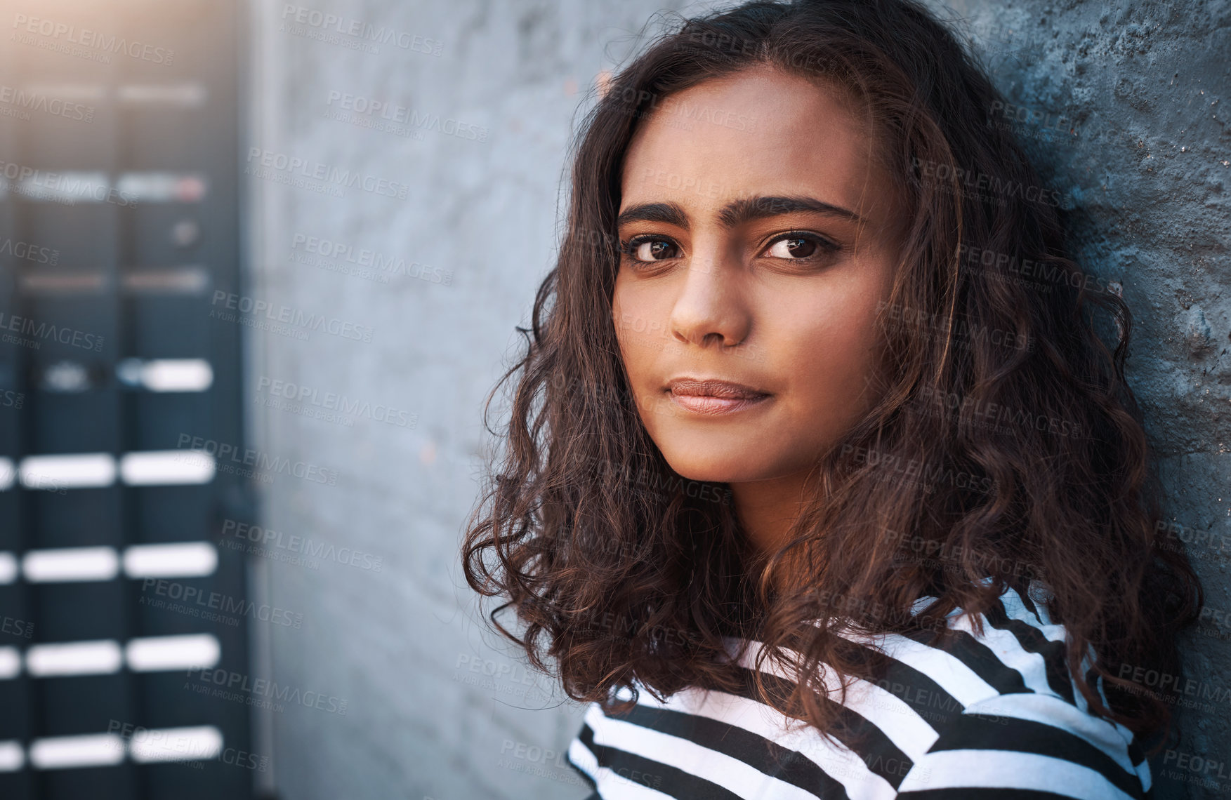 Buy stock photo Young girl, portrait and face with fashion on a wall for casual clothing or outdoor style of gen z. Indian female person or model posing with curly hair and no expression for youth in confidence