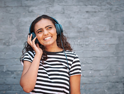 Buy stock photo Girl, headphones and smile with thinking or brick wall with music subscription, entertainment or streaming. Female person, listening and audio playlist for city travel or media, radio or connection