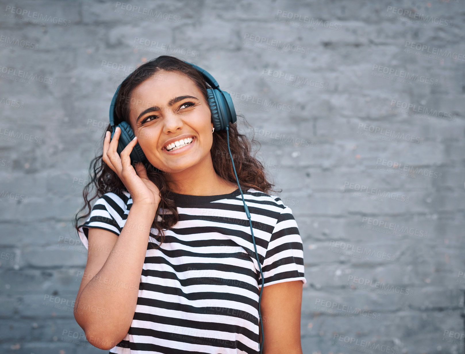 Buy stock photo Girl, headphones and smile with thinking or brick wall with music subscription, entertainment or streaming. Female person, listening and audio playlist for city travel or media, radio or connection