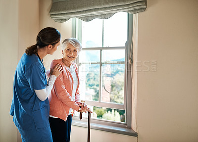 Buy stock photo Shot of a young nurse standing with a senior woman next to a window in a nursing home