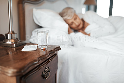 Buy stock photo Shot of pills and a glass of water with a senior woman sleeping in bed in the background