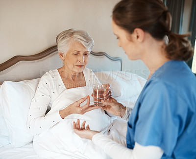 Buy stock photo Shot of a nurse giving a senior woman her medication to take with a glass of water in bed