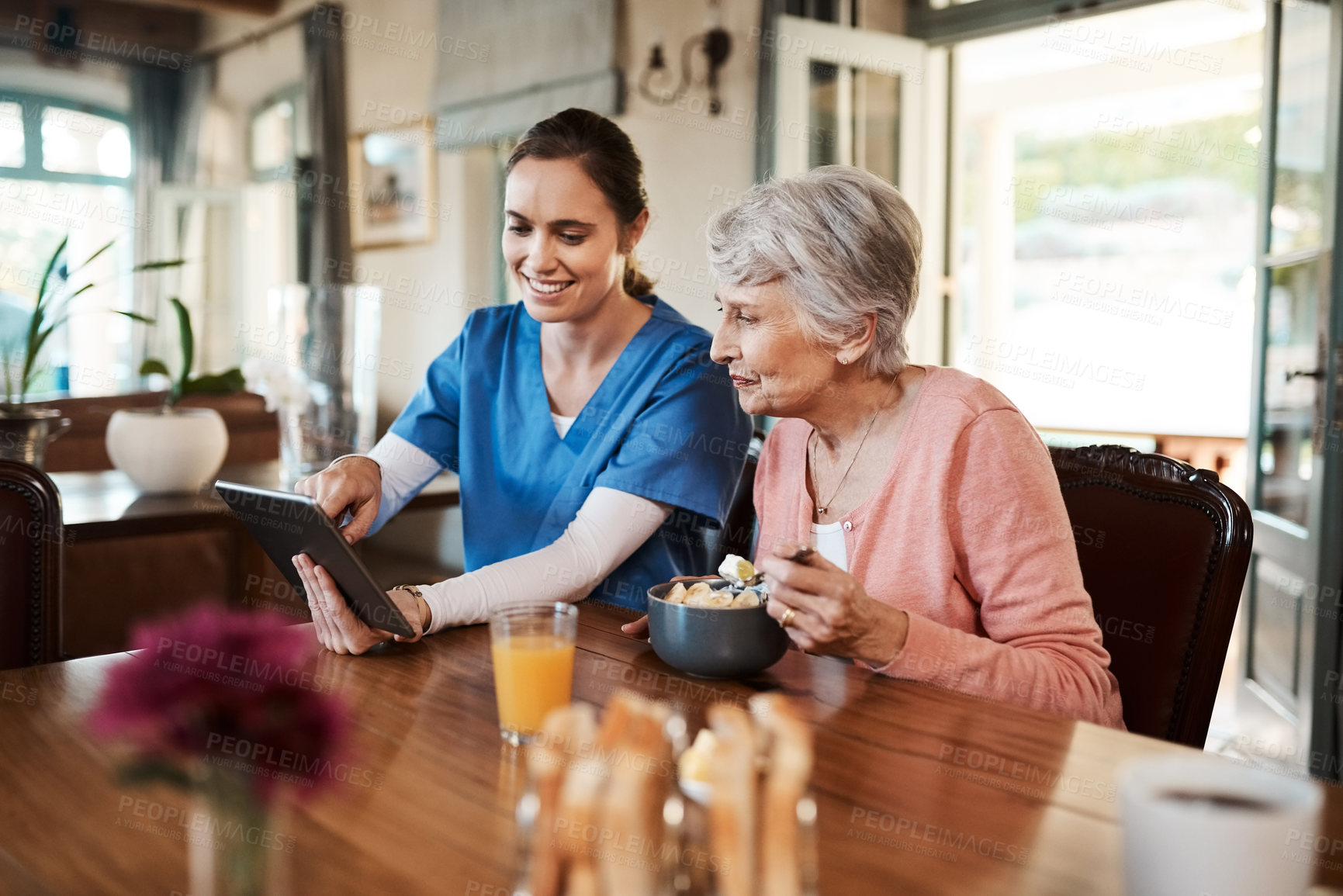 Buy stock photo Shot of a young nurse and senior woman using a digital tablet at breakfast time in a nursing home