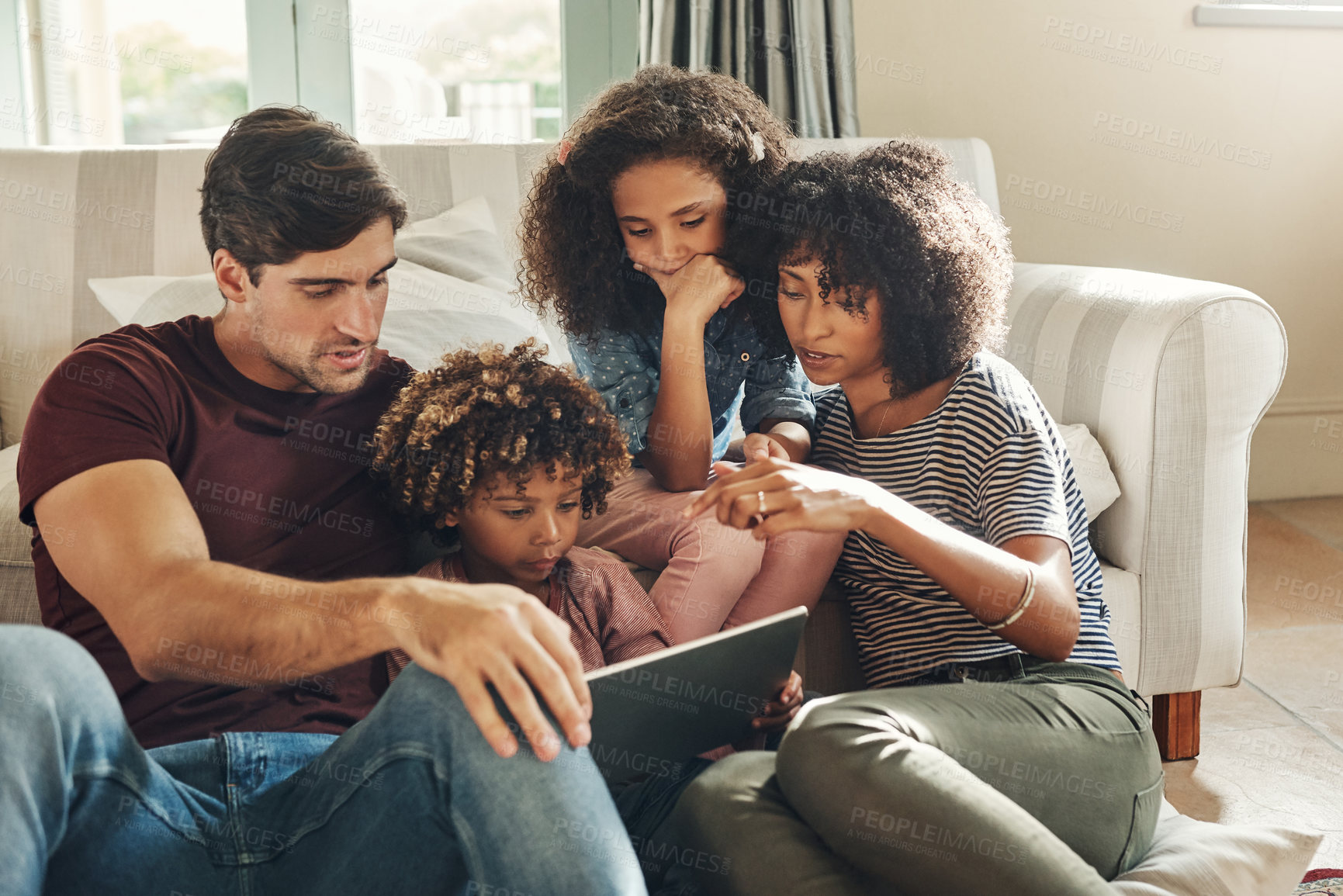 Buy stock photo Shot of a beautiful young family of four using a digital tablet together while relaxing on a sofa at home