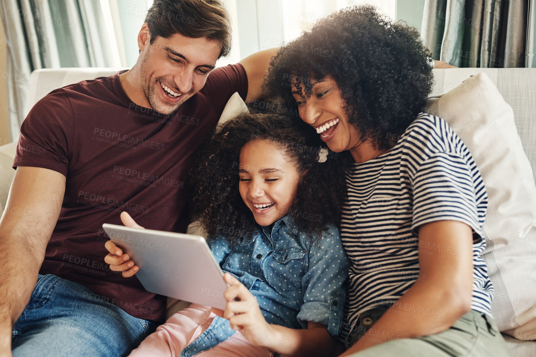 Buy stock photo Shot of a beautiful young family of three using a digital tablet while relaxing on a couch together at home