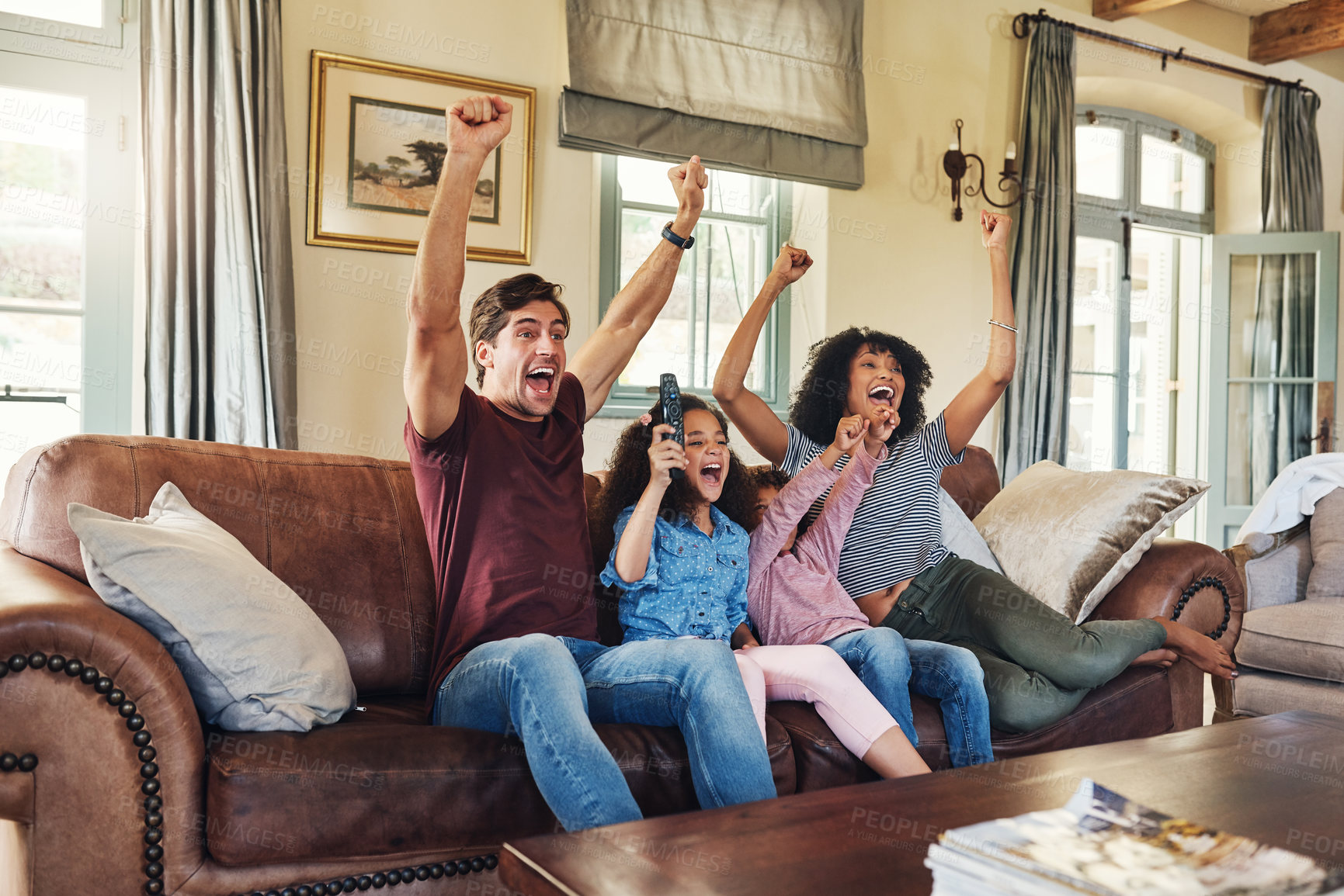 Buy stock photo Shot of a beautiful young family of four celebrating while watching tv together at home