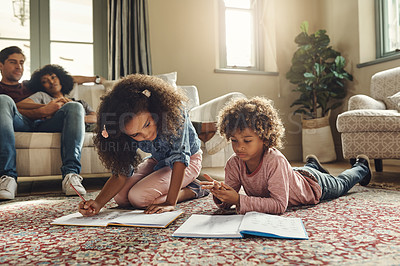 Buy stock photo Shot of two adorable young siblings doing their homework with their parents proudly watching in the background at home