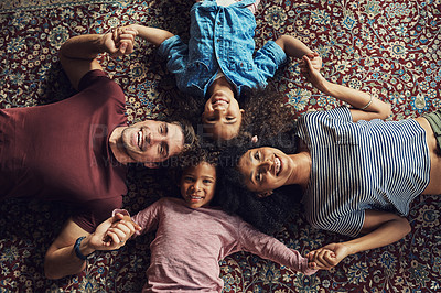 Buy stock photo High angle shot of a beautiful young family lying down on a carpet and holding hands together at home