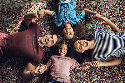 Buy stock photo High angle shot of a beautiful young family lying down on a carpet and holding hands together at home