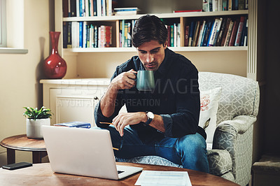 Buy stock photo Shot of a handsome young businessman drinking coffee while working on a laptop in his home office