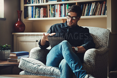 Buy stock photo Shot of a handsome young businessman using a digital tablet while working in his office at home