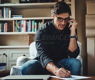 Buy stock photo Shot of a handsome young businessman making a phone call while working in his office at home