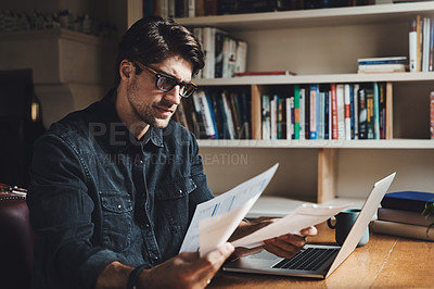 Buy stock photo Shot of a handsome young businessman going over paperwork in his office at home