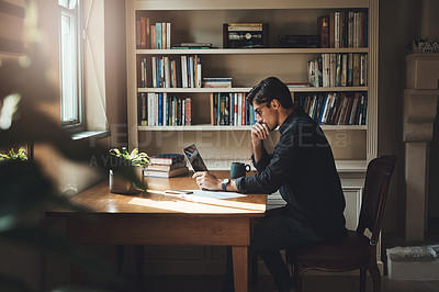 Buy stock photo Shot of a young businessman looking thoughtful while working on a laptop in his office at home