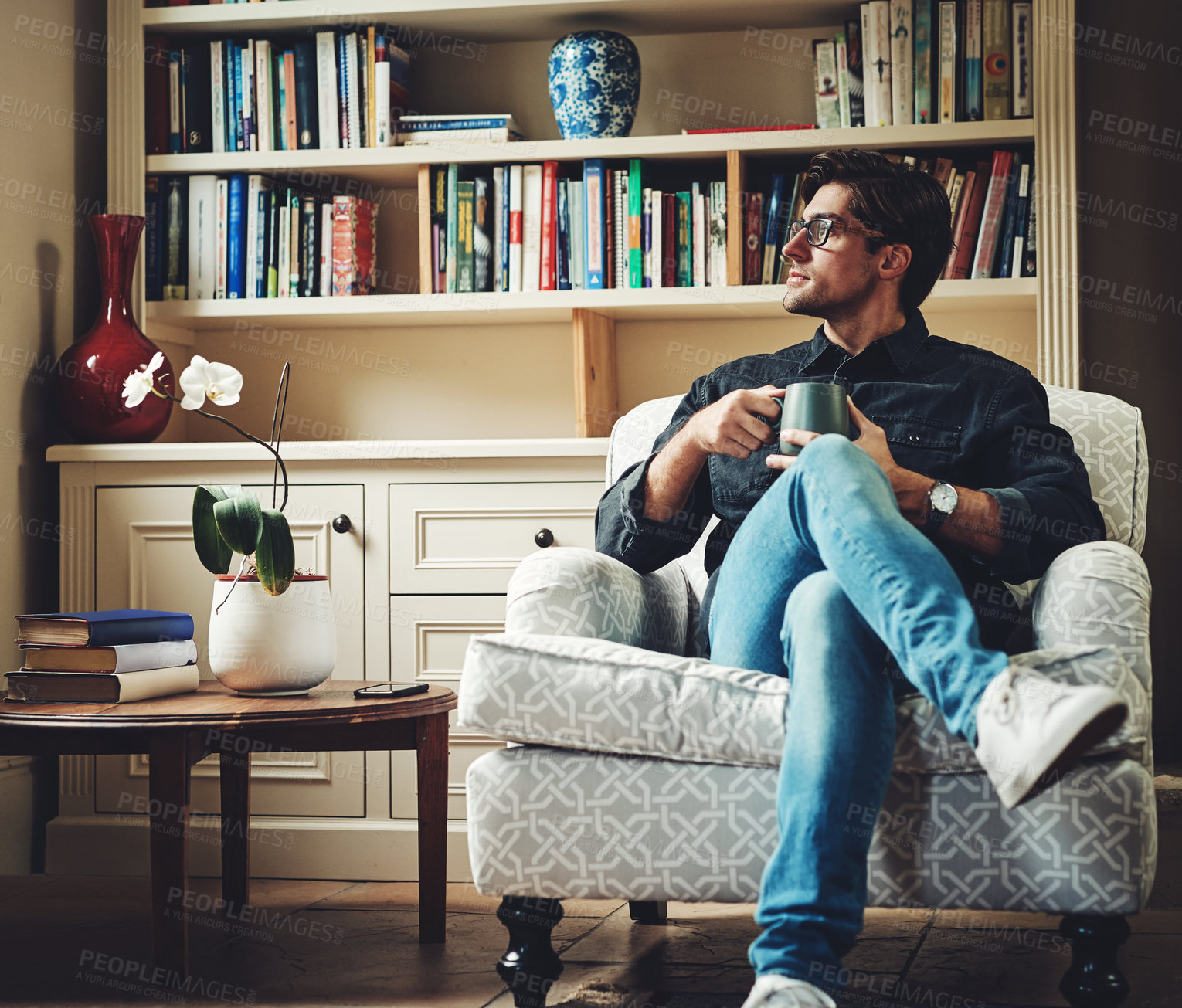 Buy stock photo Shot of a handsome young businessman drinking coffee while sitting on a couch in his office at home