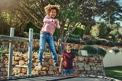 Buy stock photo Shot of an adorable little boy jumping on a trampoline with his father watching closely in the background