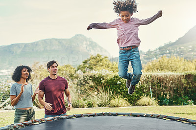 Buy stock photo Shot of an adorable little boy jumping on a trampoline with his parents watching closely in the background