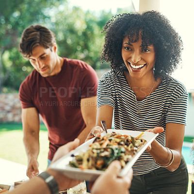 Buy stock photo Shot of a beautiful young woman passing over a plate of food at a family gathering outdoors
