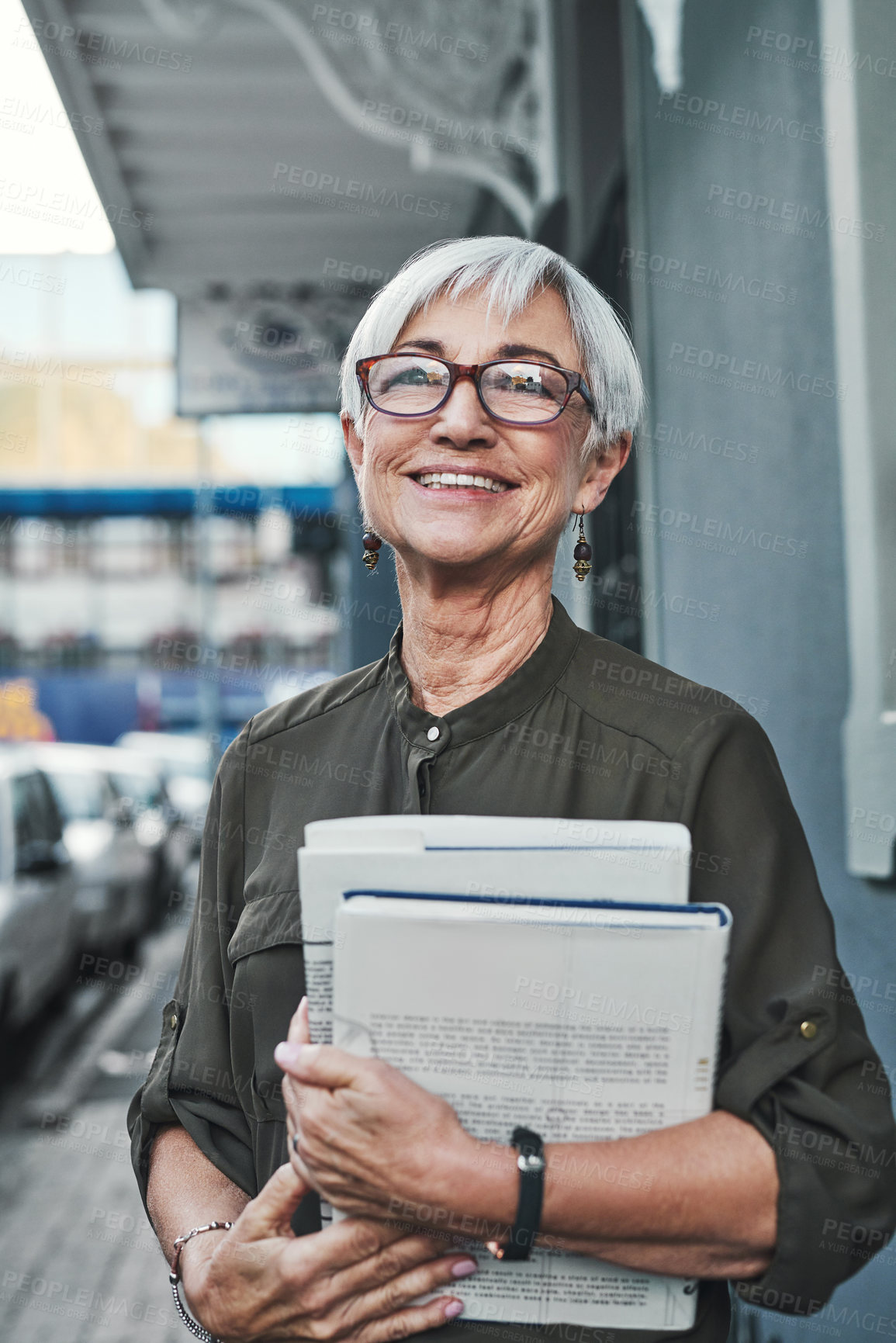 Buy stock photo Portrait of a cheerful mature businesswoman carrying books and paperwork while out in the city