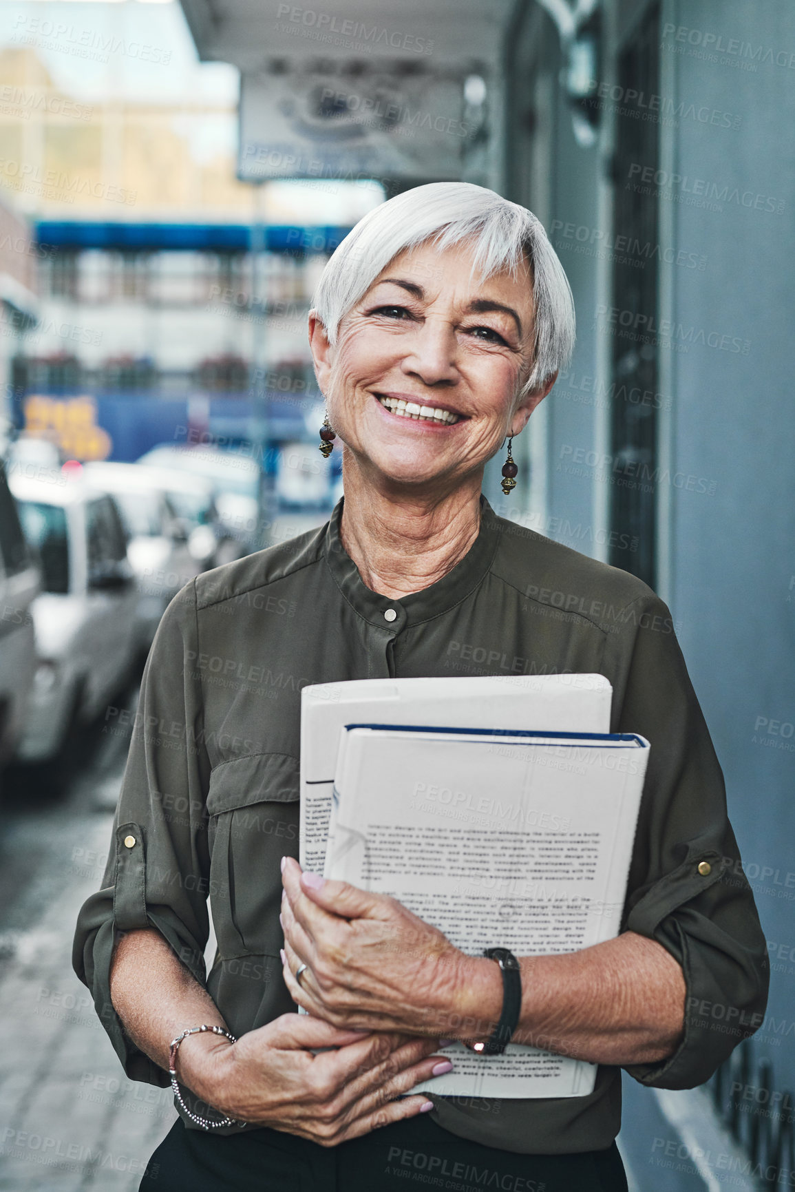 Buy stock photo Portrait of a cheerful mature businesswoman carrying books and paperwork while out in the city