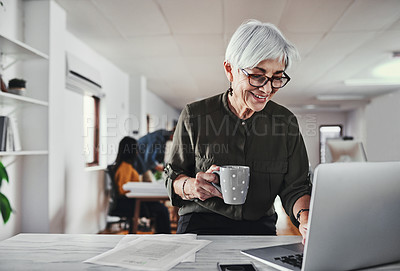 Buy stock photo Cropped shot of an attractive mature businesswoman enjoying a coffee while reading working on her laptop in the office