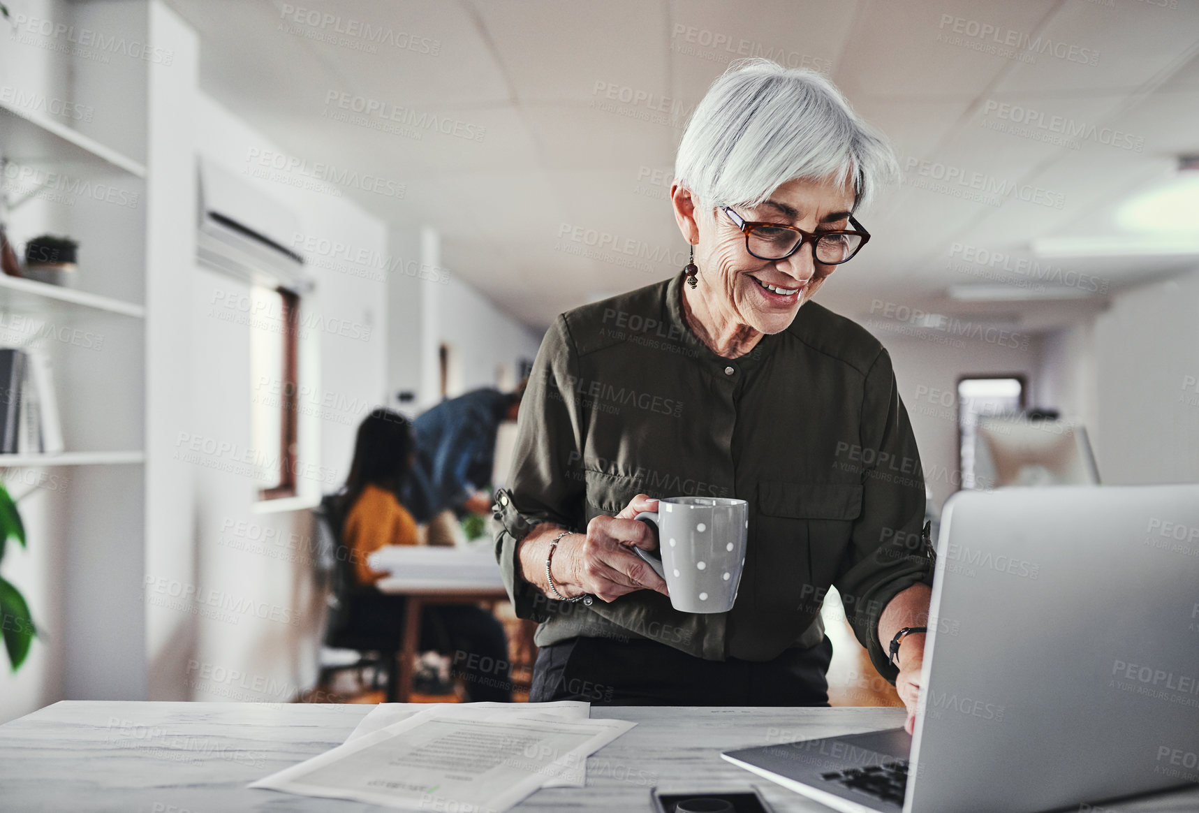 Buy stock photo Cropped shot of an attractive mature businesswoman enjoying a coffee while reading working on her laptop in the office