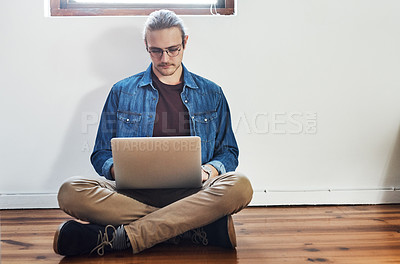 Buy stock photo Full length shot of a handsome young businessman working on his laptop while sitting on the floor in the office