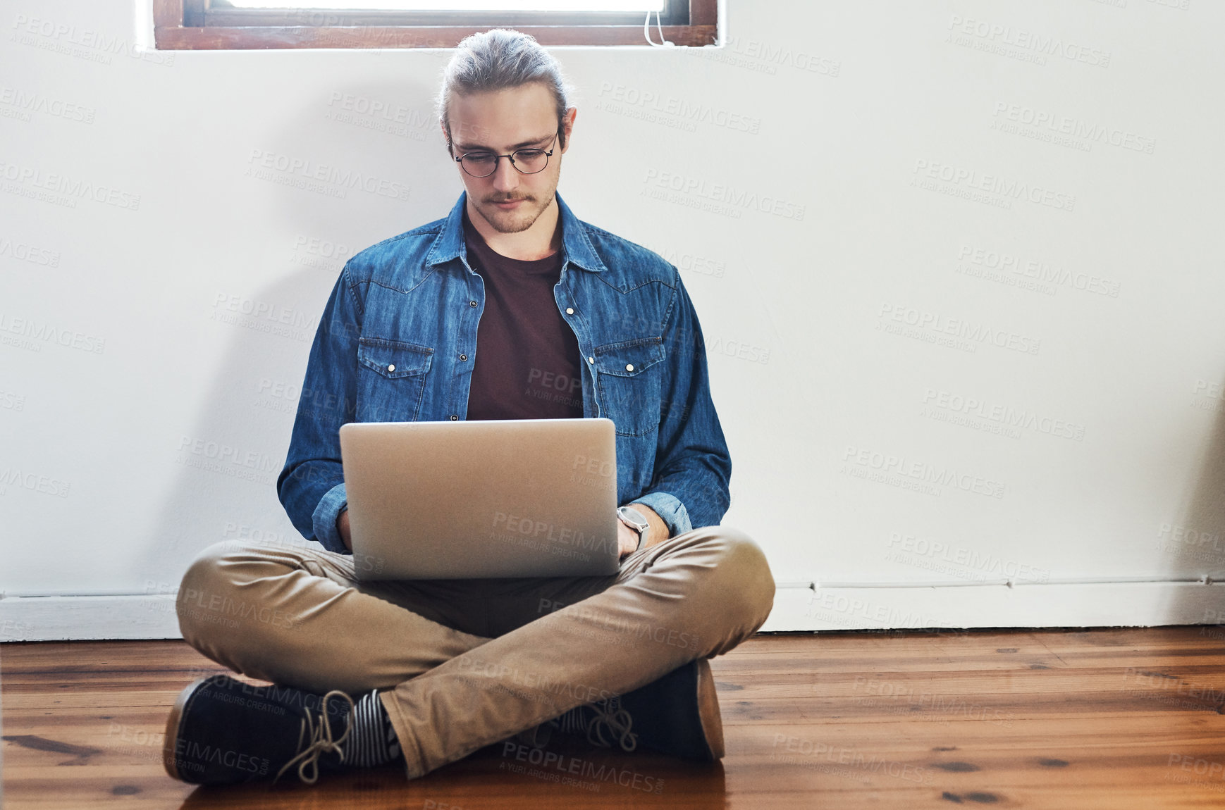 Buy stock photo Full length shot of a handsome young businessman working on his laptop while sitting on the floor in the office