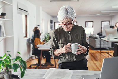Buy stock photo Cropped shot of an attractive mature businesswoman enjoying a coffee while reading through paperwork in her office