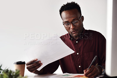 Buy stock photo Cropped shot of a handsome young businessman sitting and making notes while working with documents in the office
