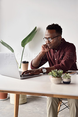 Buy stock photo Cropped shot of a handsome young businessman sitting alone and working on his laptop in the office