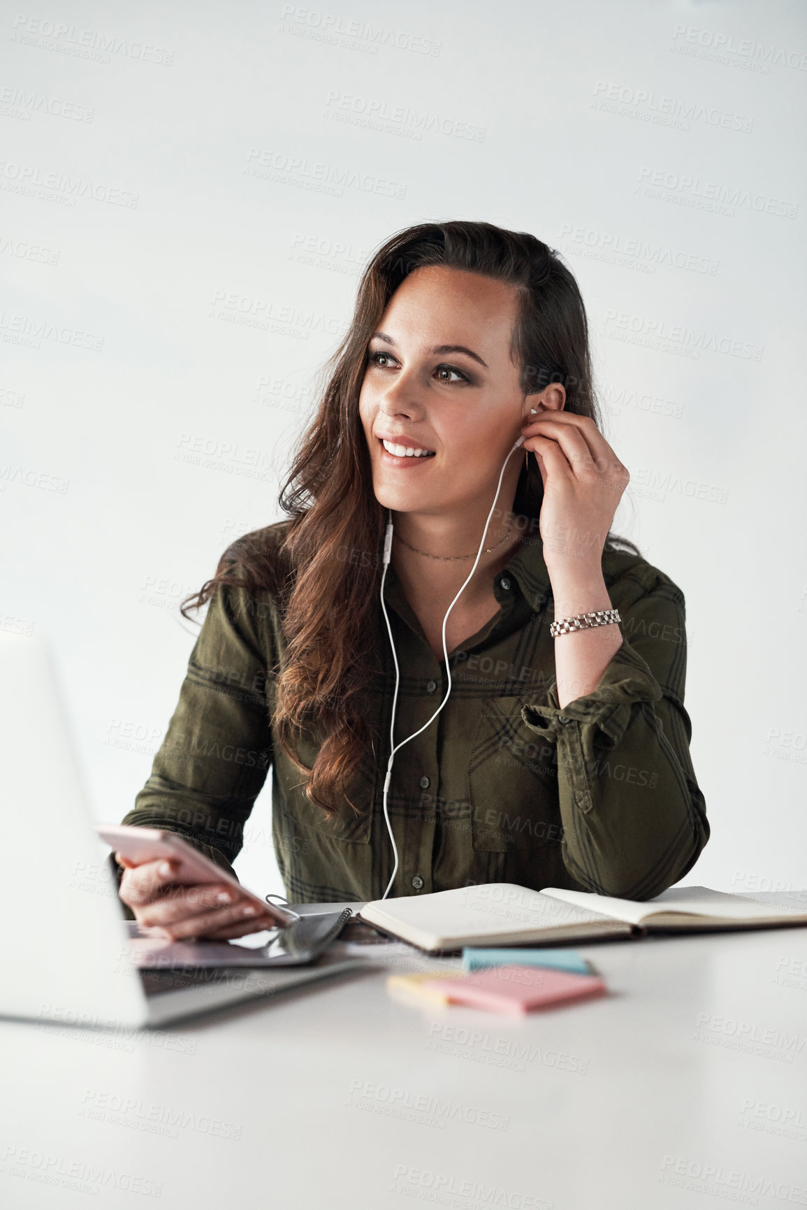 Buy stock photo Cropped shot of an attractive young businesswoman listening to music through earphones while making notes in a modern office