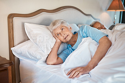 Buy stock photo Cropped shot of a contemplative senior woman lying in bed next to her sleeping husband at home
