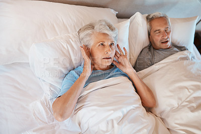 Buy stock photo Cropped shot of a senior woman blocking her ears in frustration while her husband snores in bed beside her