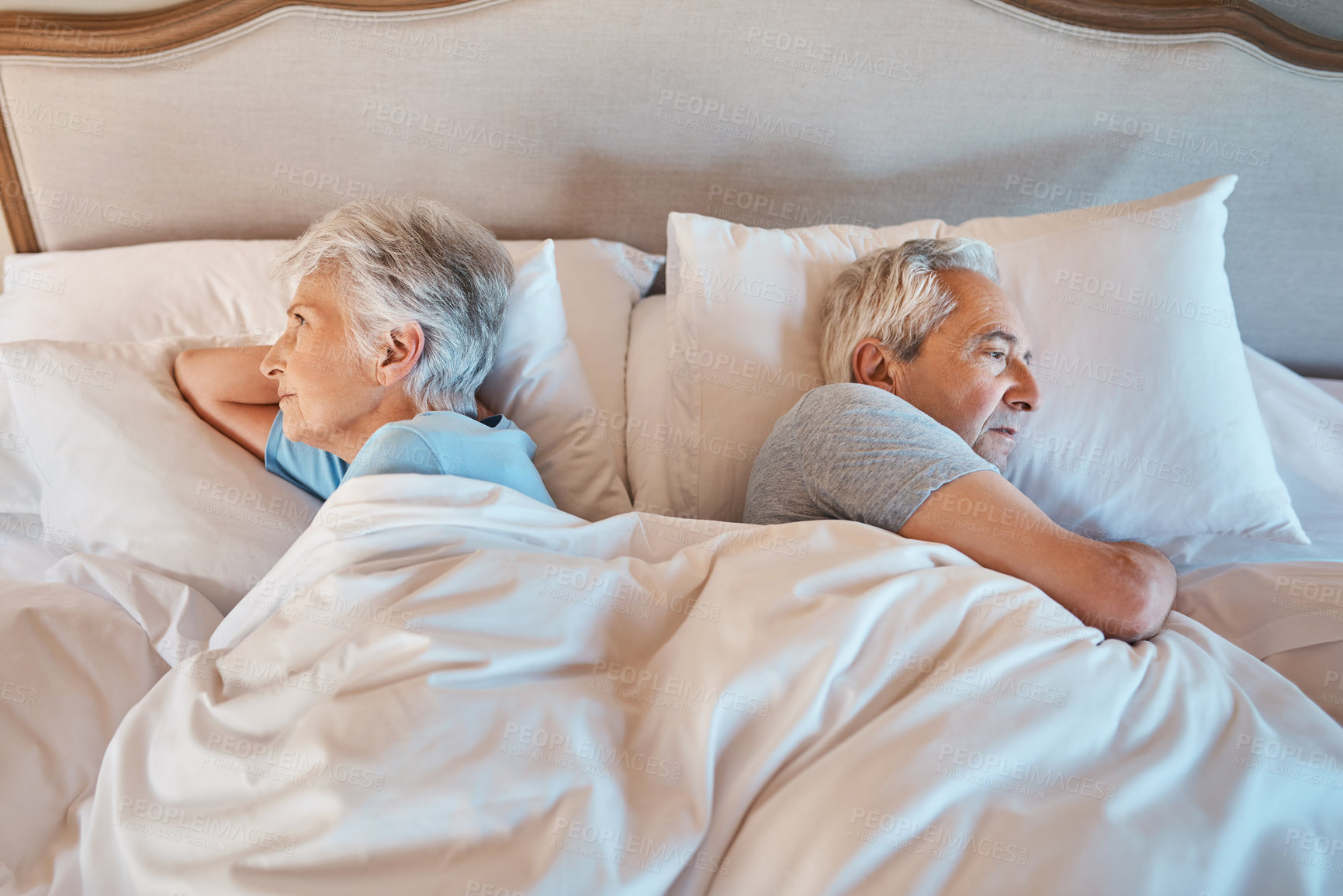 Buy stock photo Cropped shot of an unhappy senior couple lying away from each other in bed during a disagreement at home