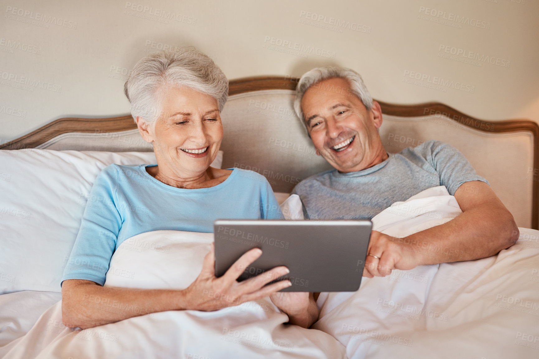 Buy stock photo Cropped shot of a happy senior couple sitting together in bed and using a tablet in a nursing home