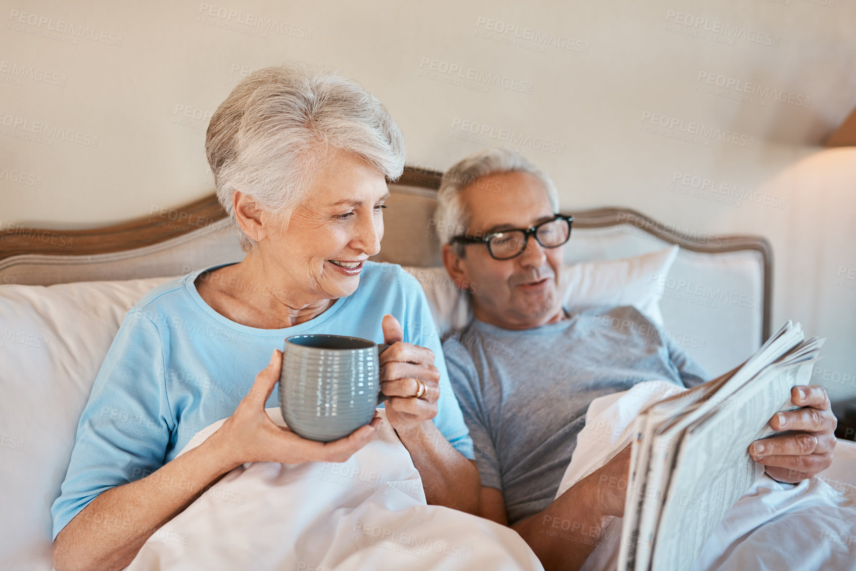 Buy stock photo Cropped shot of a senior man reading a newspaper in bed while his wife drinks a cup of coffee