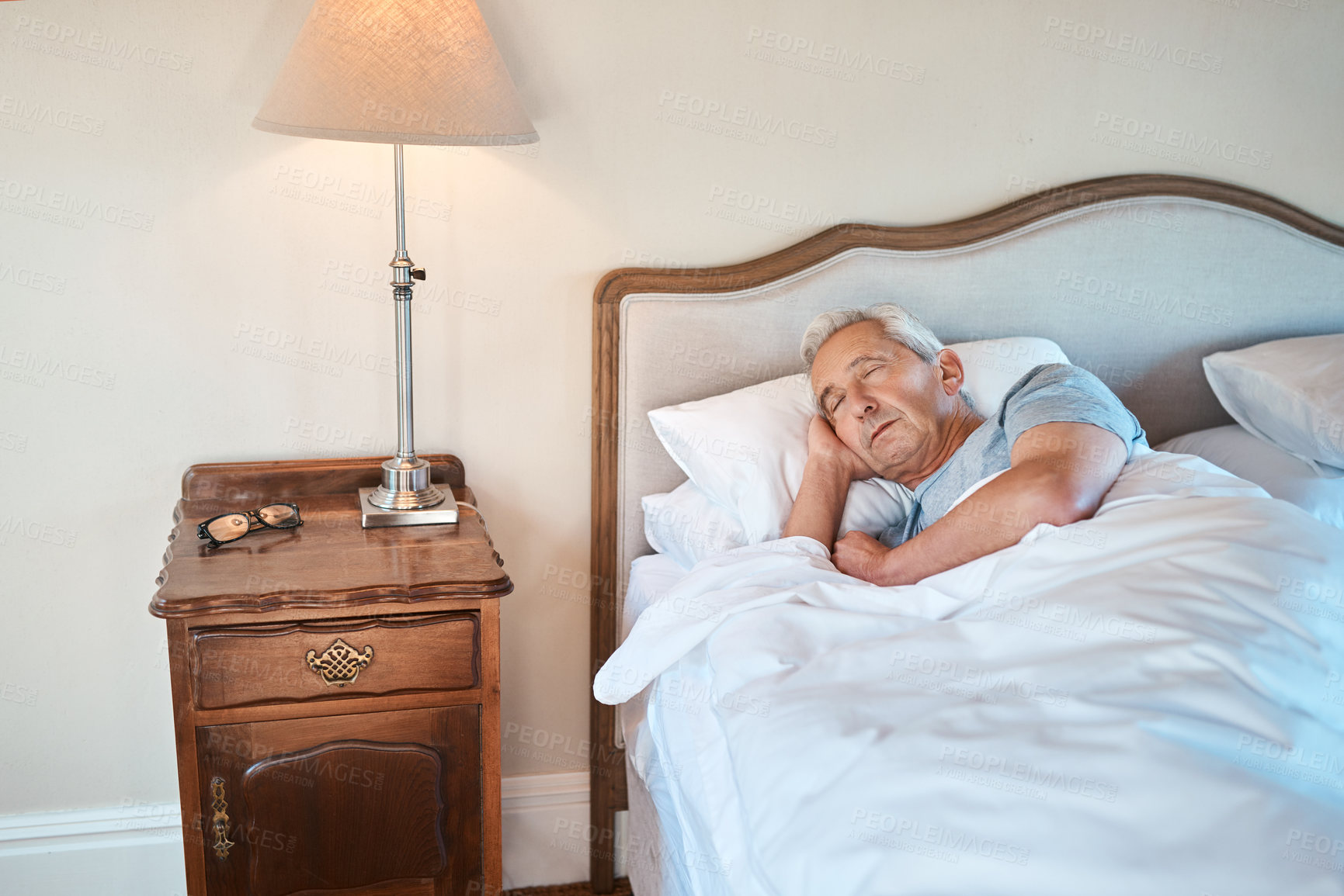 Buy stock photo Senior man, sleeping and bed with lamp light for morning, rest or recovery in retirement home. Elderly, male person or asleep with blankets, sheets or duvet by pedestal for relaxation in bedroom