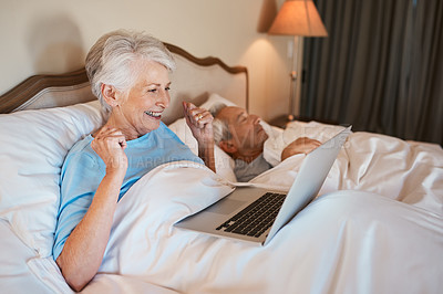 Buy stock photo Cropped shot of a senior woman sitting in bed and using a laptop while her husband sleeps beside her