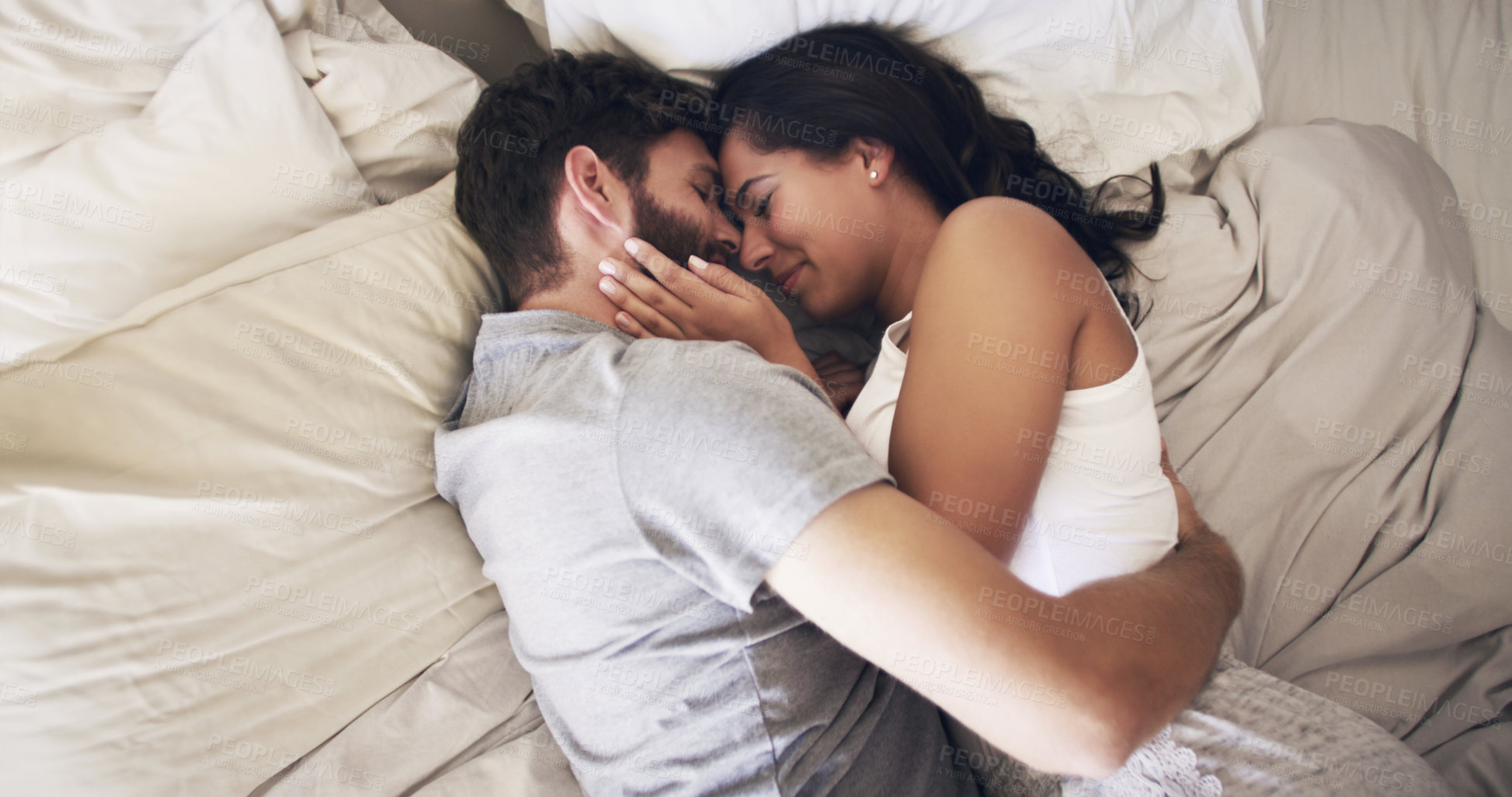 Buy stock photo Shot of an affectionate young couple embracing in bed at home